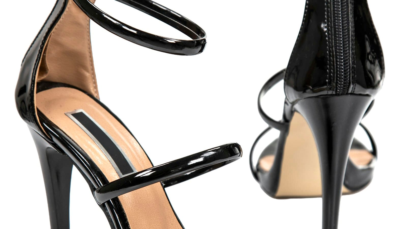 Two black patent leather high heel sandals with ankle straps on white