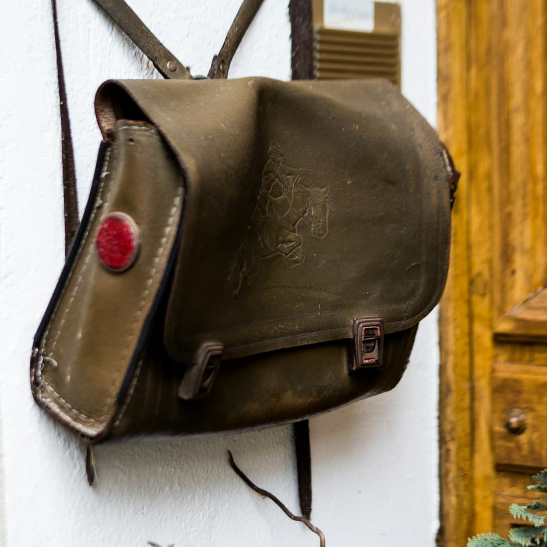 A vintage olive green satchel hangs on a wall