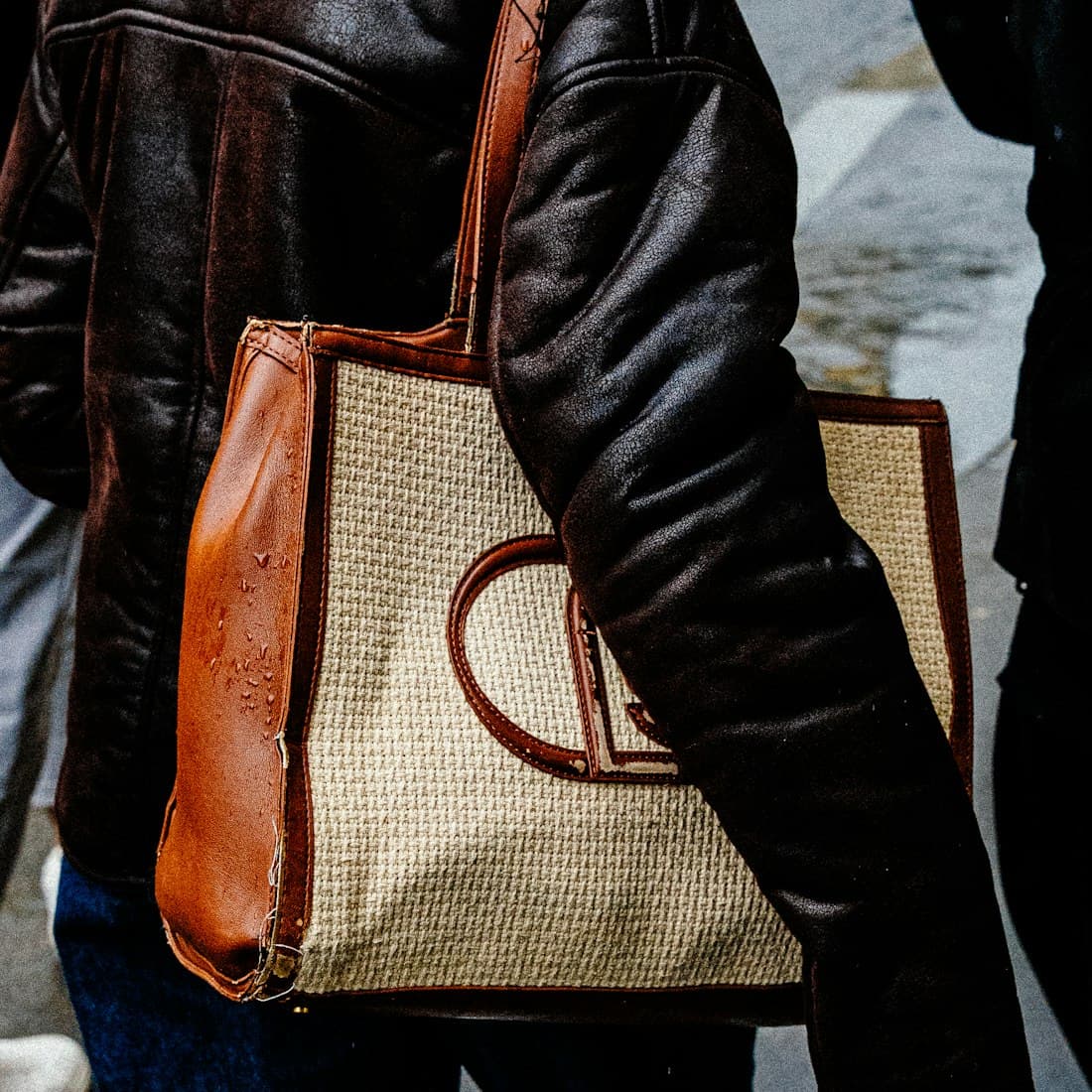 Woman in a leather jacket carries a tote bag