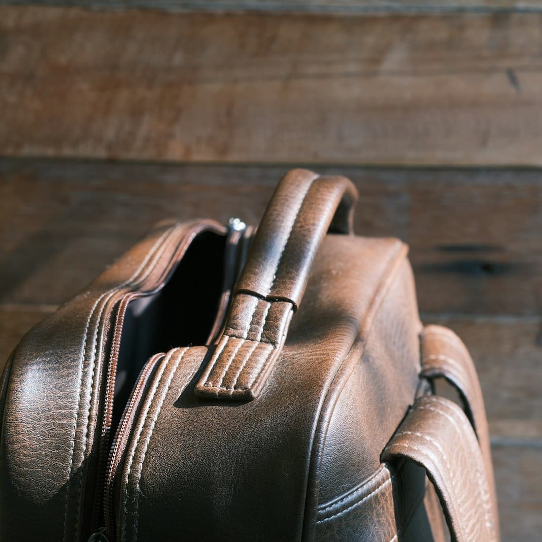 A brown leather backpack sitting on top of a wooden floor
