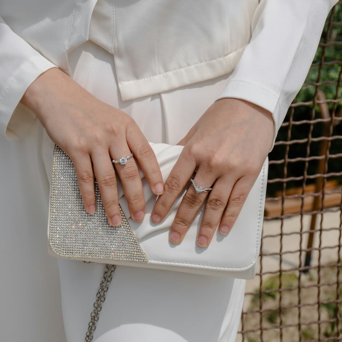 Hands holding a white beaded clutch bag with rings